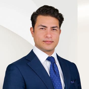 Navid Hashemi in einem blauen Anzug und einer gepunkteten Krawatte, der vor einem hellen, abstrakten Hintergrund steht.