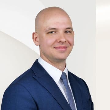 Jonas Friesse in blauem Anzug und Krawatte vor einem hellen, abstrakten Hintergrund.