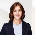 Headshot of a smiling woman with brown hair, wearing a blue blazer and striped shirt.
