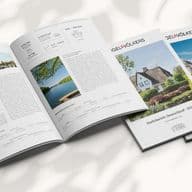 Geöffnete und geschlossene Immobilienbroschüren auf einem hellen Untergrund mit Schatten, mit Immobilienangeboten und Landschaftsfotos