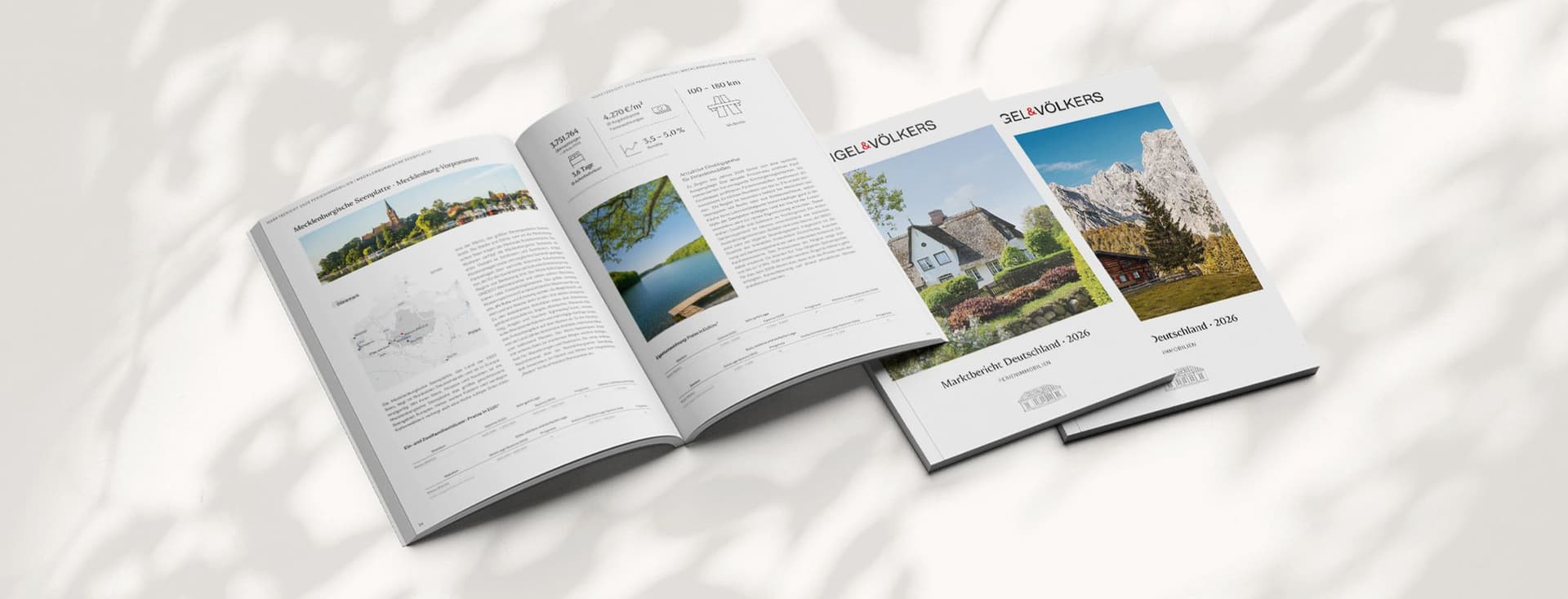Geöffnete und geschlossene Immobilienbroschüren auf einem hellen Untergrund mit Schatten, mit Immobilienangeboten und Landschaftsfotos