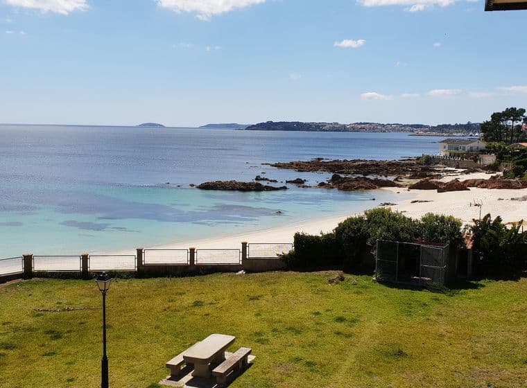 Vista de la platja d'Areas amb Sanxenxo al fons. Es veu un parc amb una taula, la platja al mig i Sanxenxo a l'horitzó.