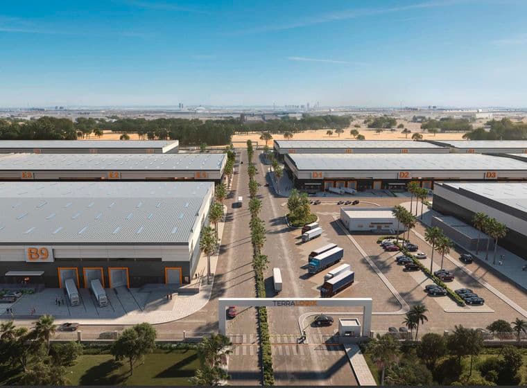 Aerial view of a modern industrial park with large warehouse buildings, trucks, parked cars, and a central entrance gate marked "TERRA LOGYX."