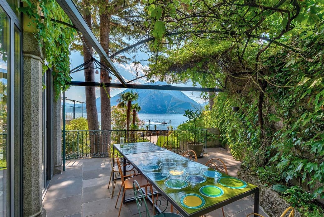 Überdachte Terrasse mit Essbereich, umgeben von Grünpflanzen, mit Blick auf den Comer See