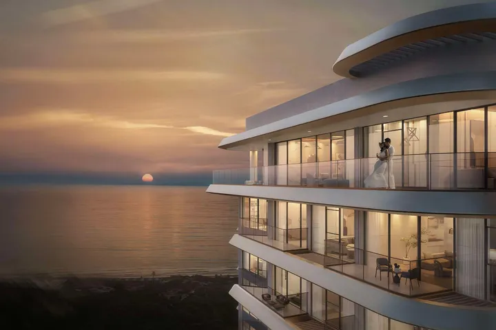 Sunset over the ocean beside a futuristic curved glass building; a bride and groom stand on an illuminated balcony.