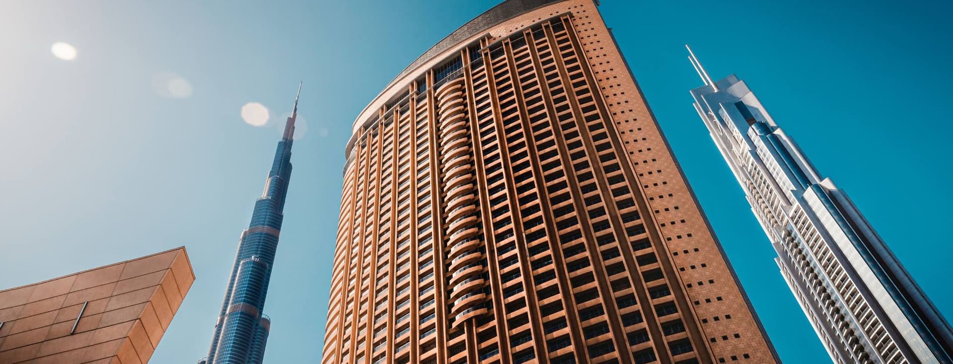 Skyscrapers under a clear blue sky, including a tall, iconic tower and a modern building with a curved facade, viewed from below.