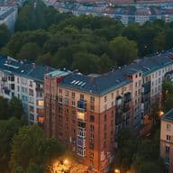Aerial view of colorful apartment buildings surrounded by trees in a city at dusk, with streetlights glowing softly.