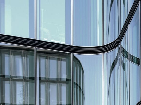 Eine geschwungene, moderne Glasfassade, in der sich die umliegenden Gebäude in sanften, wellenförmigen Mustern spiegeln.