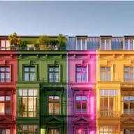 Eine Reihe bunter Berliner Reihenhäuser mit Balkonen und Dachgärten, wobei jedes Gebäude in einer anderen Farbe gestrichen ist und von Bäumen eingerahmt wird.