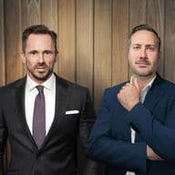 Benjamin Rogmans und Michael Gassmann in eleganten Anzügen stehen selbstbewusst vor einer holzgetäfelten Wand und strahlen eine professionelle und gelassene Haltung aus.