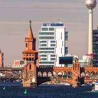 Die Oberbaumbrücke in Friedrichshain über der Spree vor einer modernen Stadtkulisse, im Hintergrund ein Fernsehturm und verschiedene architektonische Stile.
