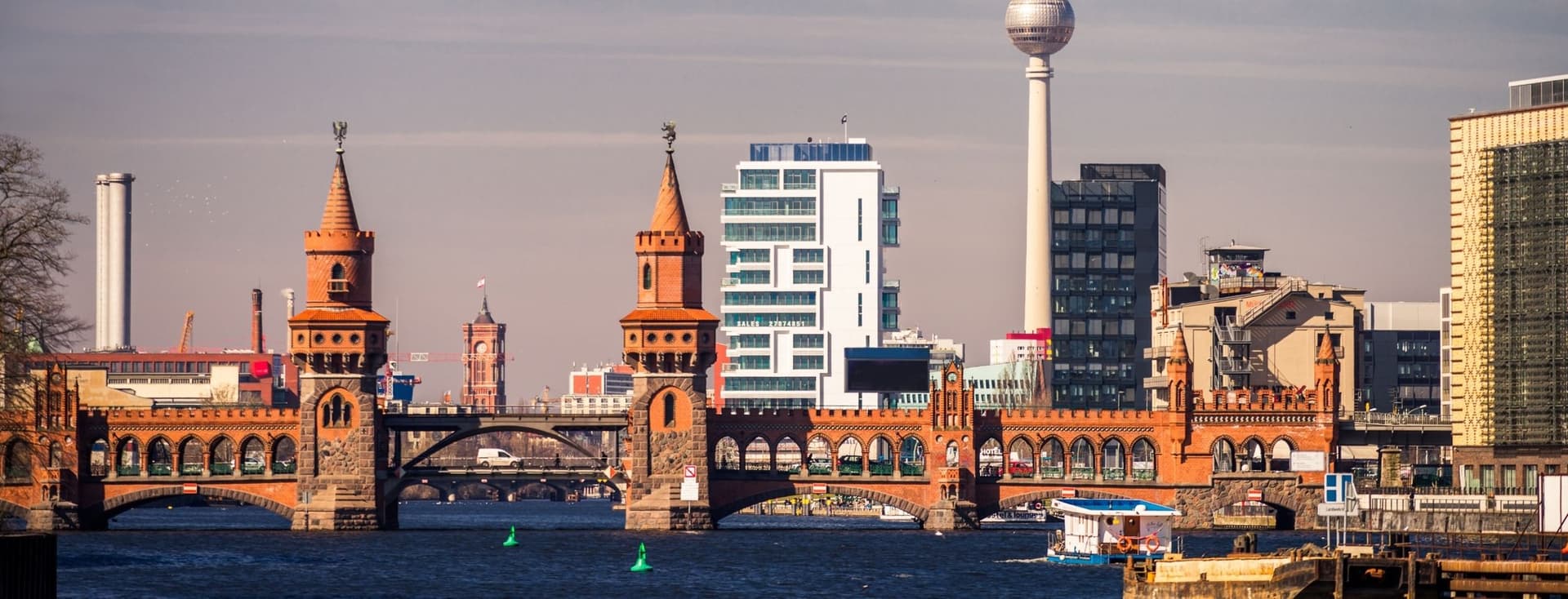 Die Oberbaumbrücke in Friedrichshain über der Spree vor einer modernen Stadtkulisse, im Hintergrund ein Fernsehturm und verschiedene architektonische Stile.