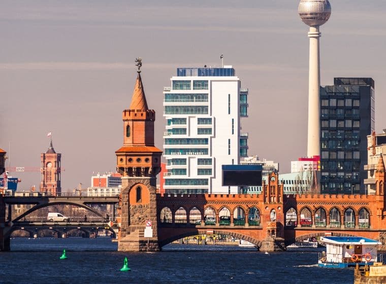 Die Oberbaumbrücke in Friedrichshain über der Spree vor einer modernen Stadtkulisse, im Hintergrund ein Fernsehturm und verschiedene architektonische Stile.