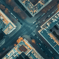Aerial view of a city intersection, surrounded by illuminated buildings and streets, with a grid-like pattern, captured at dusk.