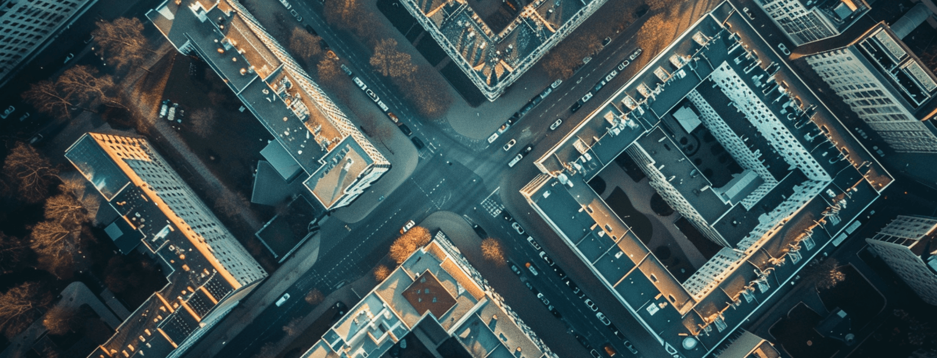 Aerial view of a city intersection, surrounded by illuminated buildings and streets, with a grid-like pattern, captured at dusk.