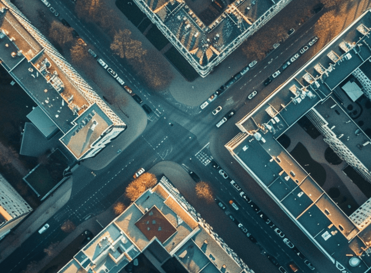 Aerial view of a city intersection, surrounded by illuminated buildings and streets, with a grid-like pattern, captured at dusk.