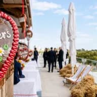 EXPO LOKAL Veranstaltung auf der Dachterrasse mit überdimensionalen Lebkuchenherzen, auf denen „Engel & Völkers“ und „EXPO Lokal Berlin“ zu lesen ist; die Gäste unterhalten sich inmitten von Sonnenblumen und Heuballen.