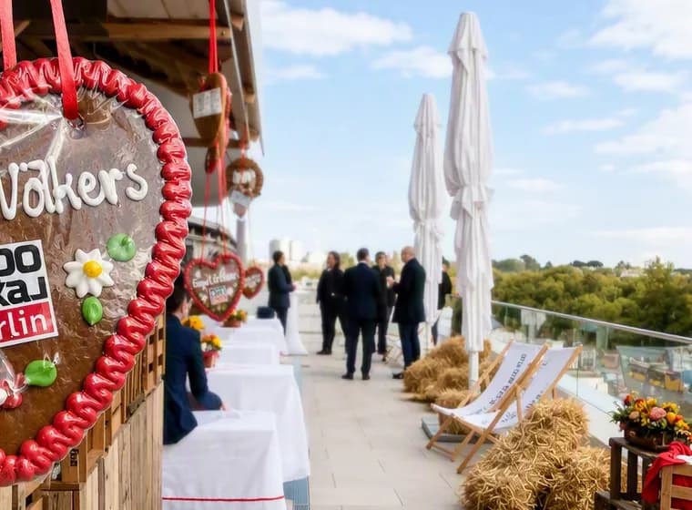 EXPO LOKAL Veranstaltung auf der Dachterrasse mit überdimensionalen Lebkuchenherzen, auf denen „Engel & Völkers“ und „EXPO Lokal Berlin“ zu lesen ist; die Gäste unterhalten sich inmitten von Sonnenblumen und Heuballen.