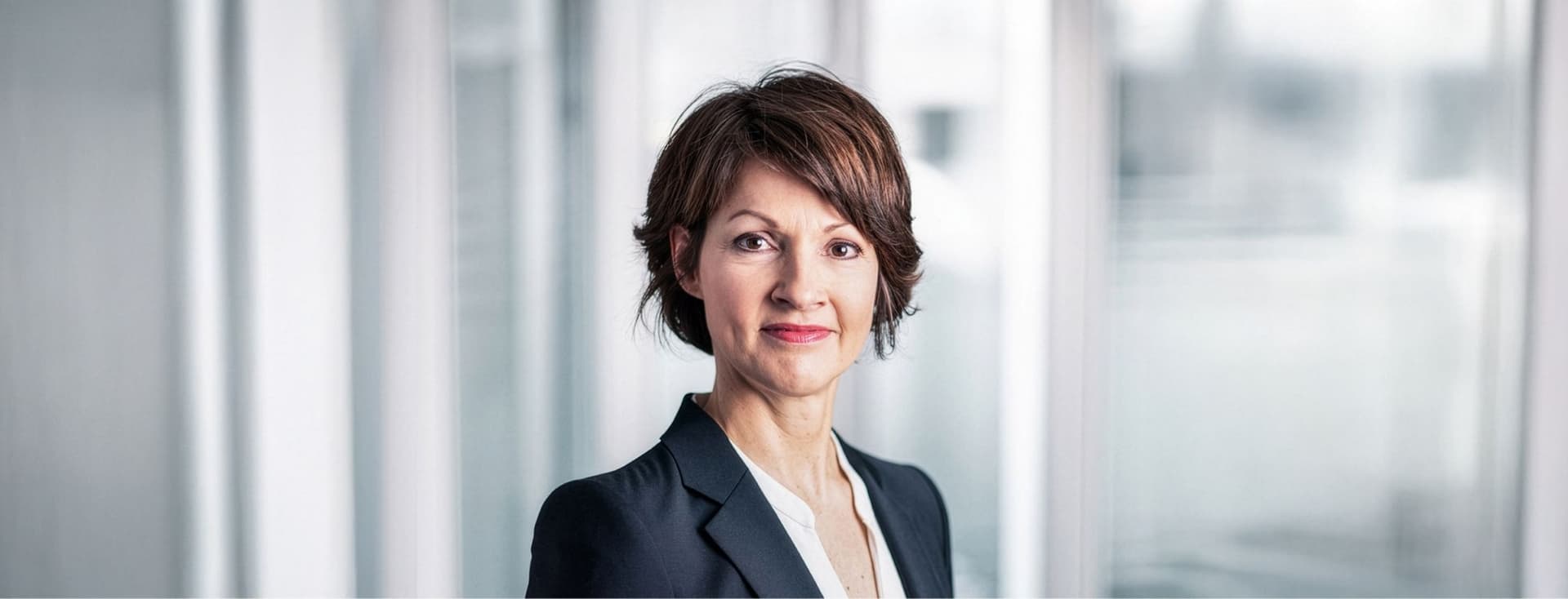 Dr. Andrea Peters mit kurzen braunen Haaren in einem schwarzen Blazer und einer weißen Bluse vor einem unscharfen, hellen Hintergrund.
