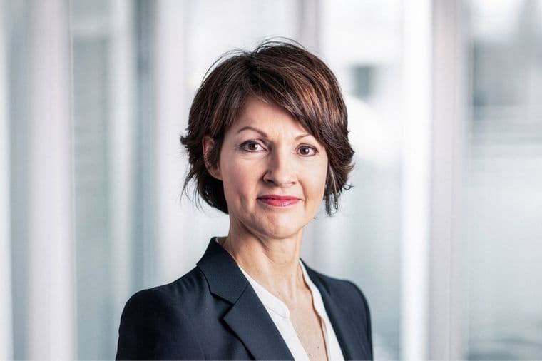Dr. Andrea Peters mit kurzen braunen Haaren in einem schwarzen Blazer und einer weißen Bluse vor einem unscharfen, hellen Hintergrund.