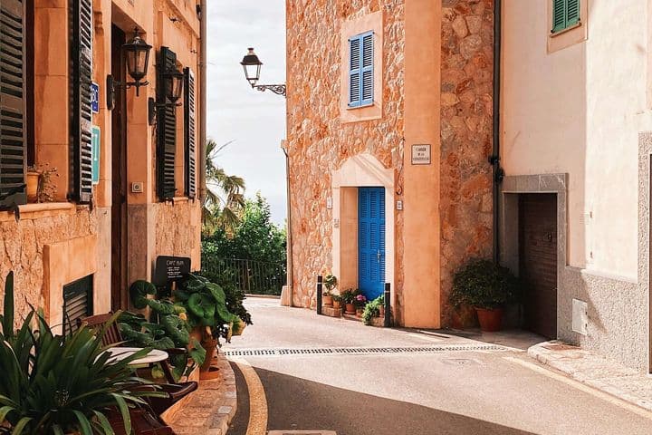 Man sieht Steinhäuser mit Fensterläden, links im Bild Pflanzen vor einem Gebäude.