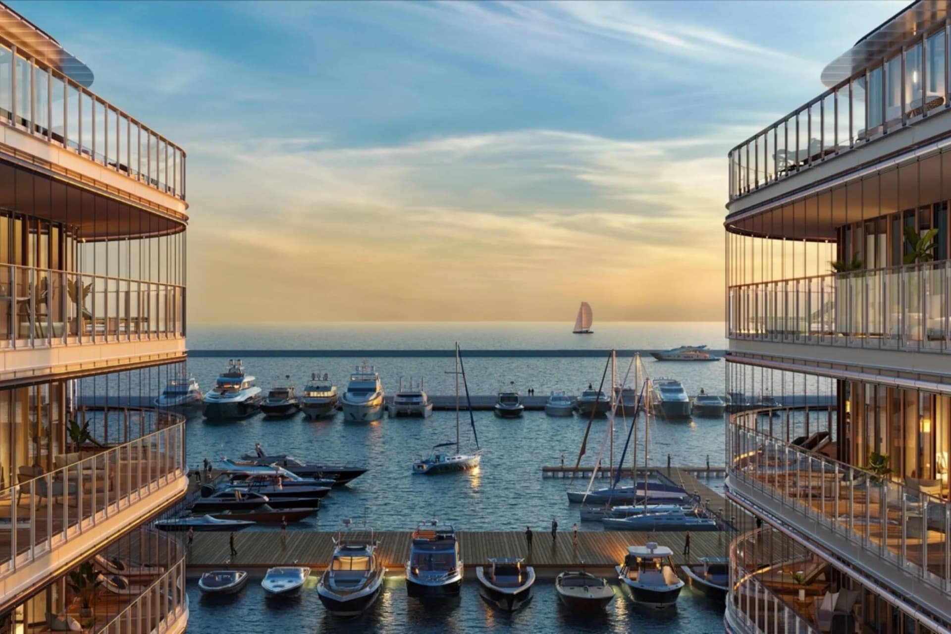 A view of the sunset over a marina, framed by curved glass buildings, with numerous yachts moored in the calm waters and a sailing boat in the distance