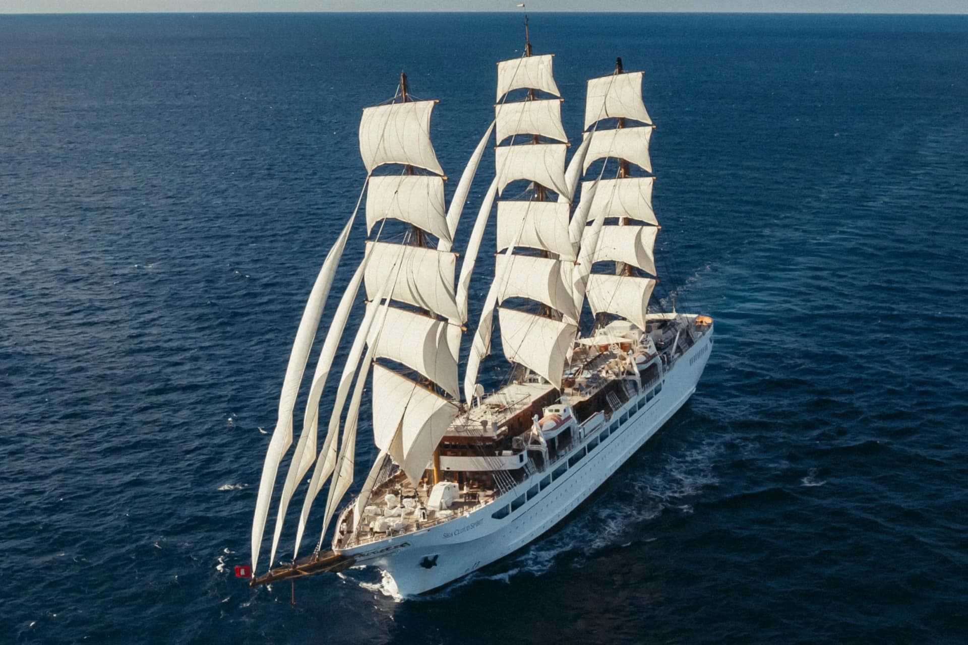 A white, multi-masted sailing ship with square sails, sailing on the deep blue sea.