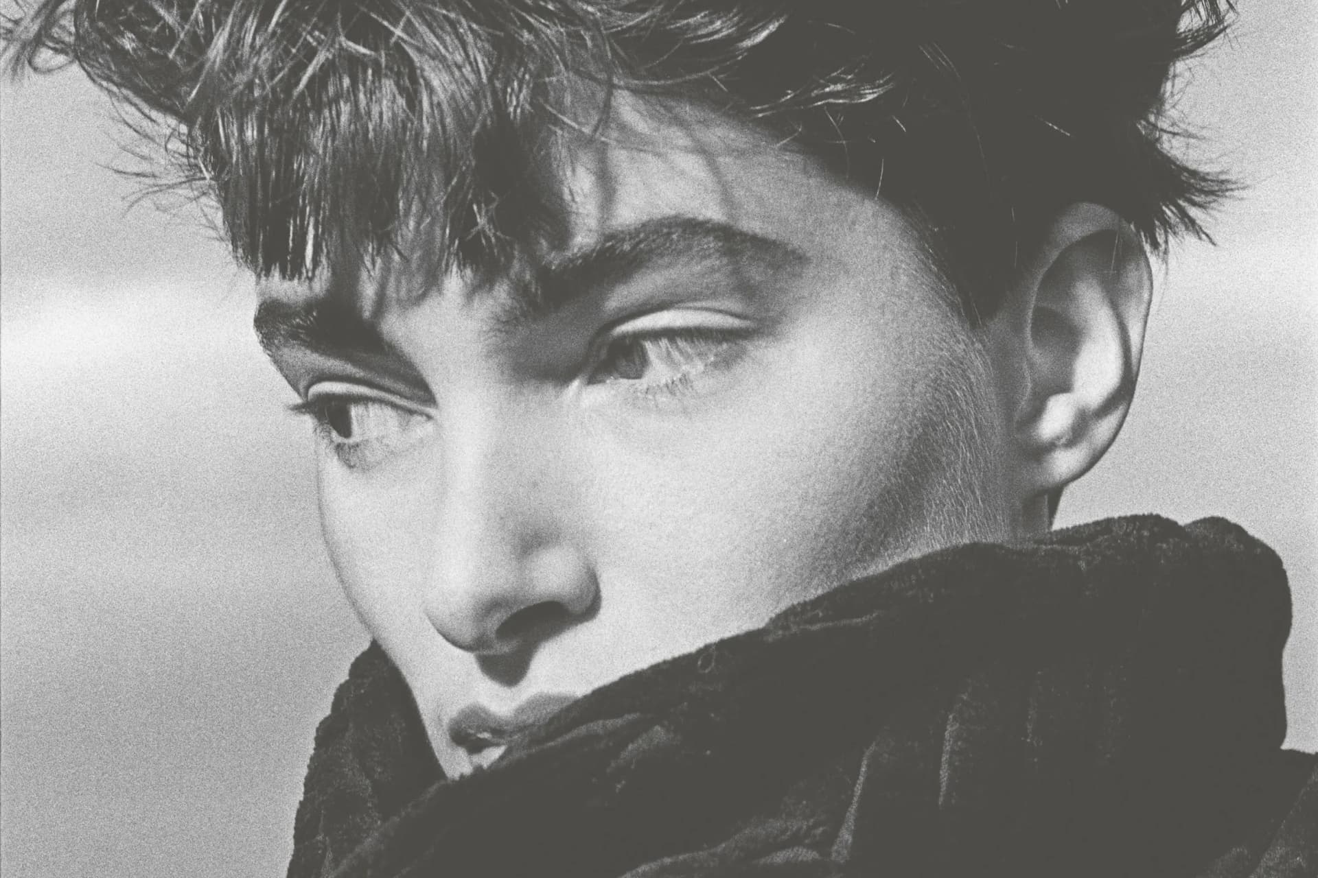Black-and-white close-up of a young woman with messy hair, eyes looking downward, wrapped in a dark scarf covering his mouth.