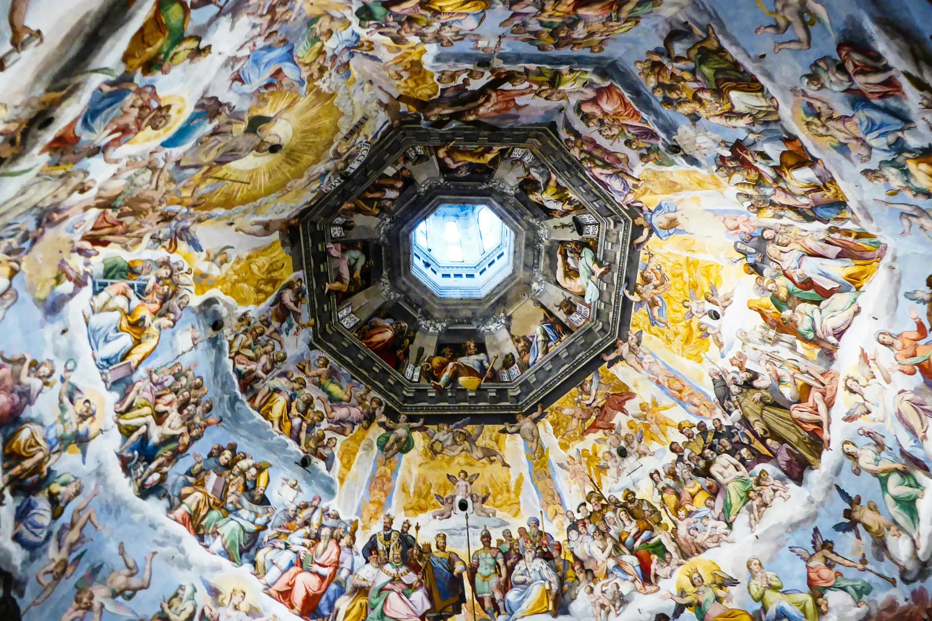 Colorful Renaissance frescoes cover a domed ceiling, filled with angels and saints around a central octagonal skylight revealing blue sky.