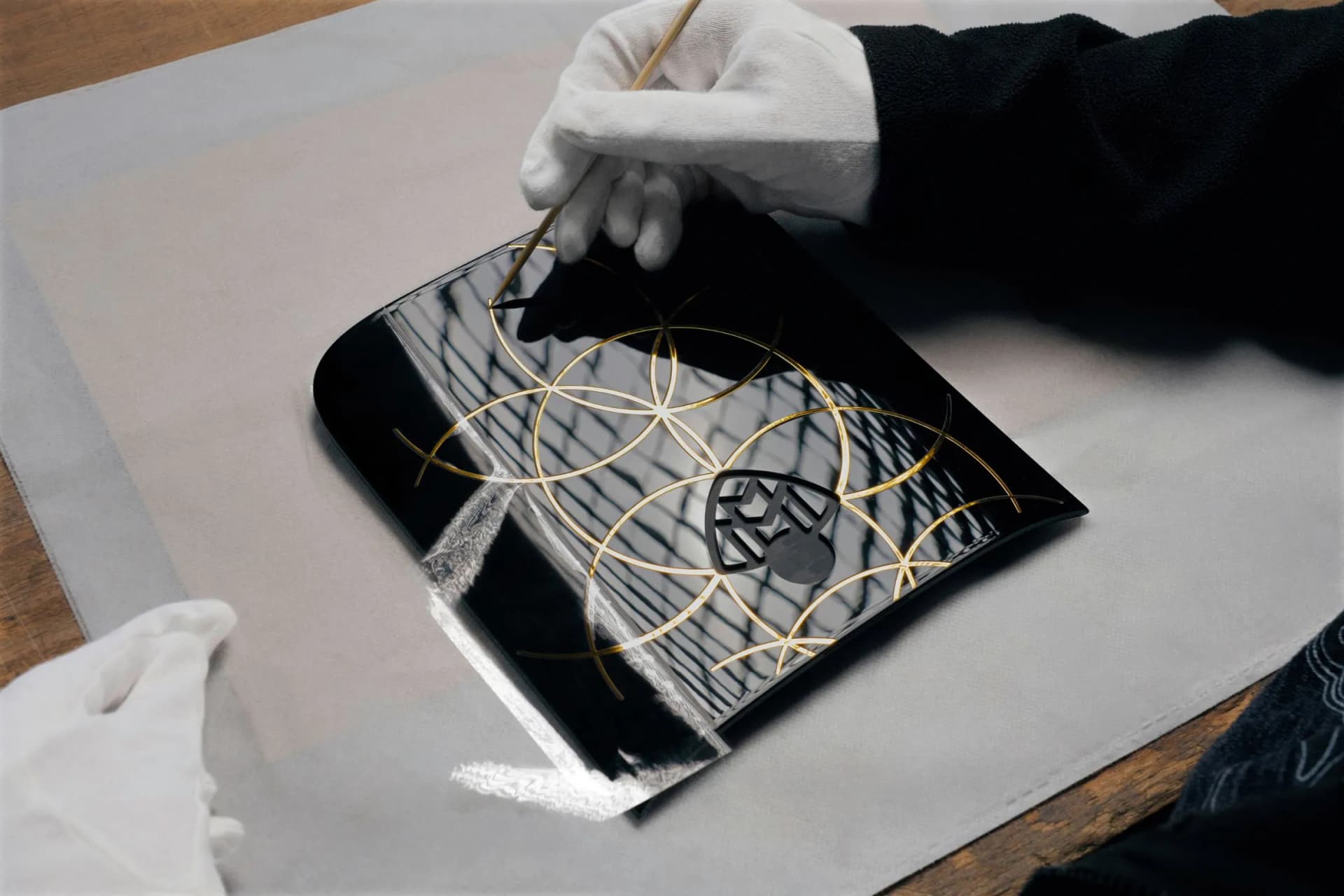A hand in a glove is using a thin tool to arrange golden circular patterns on the glossy black cover of a magazine.