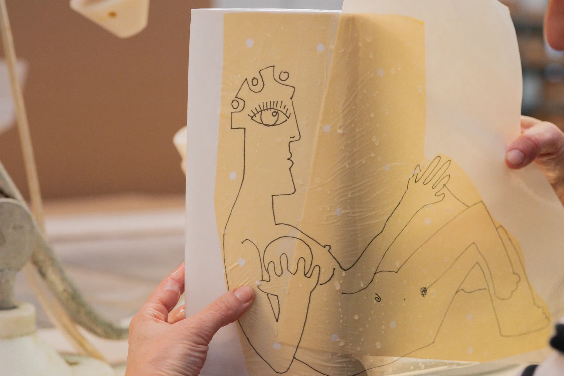 A translucent sheet shows a minimalist line drawing of a crowned figure with an eye on its head and raised hands.