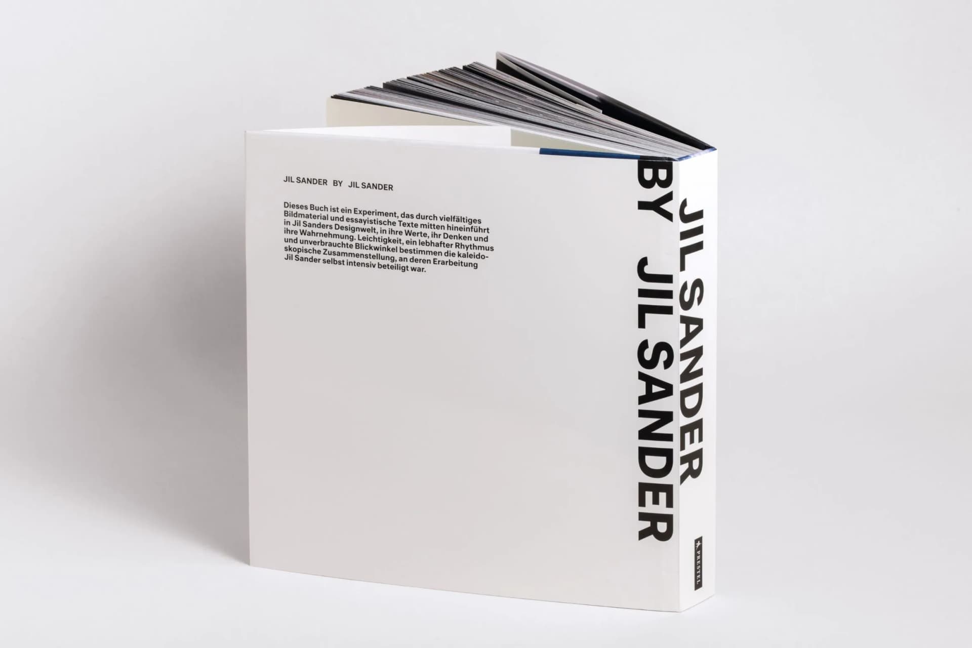 White book with bold vertical text BY JIL SANDER along the right edge and fanned dark pages at the top.