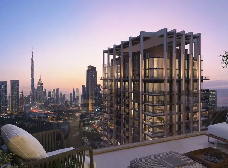 Rooftop terrace view of a modern cityscape at sunset, featuring a tall glass building and a distant skyline with skyscrapers.