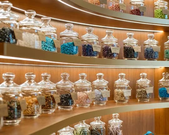 Curved wooden shelves lined with glass jars full of colorful beads, each labeled with a tag.