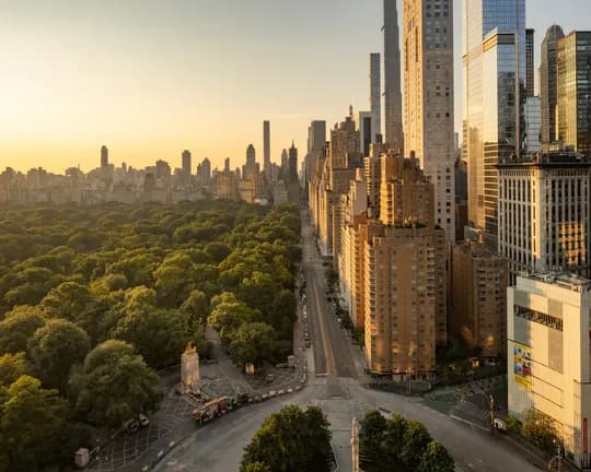 Panoramic city skyline at sunset with golden light reflecting off tall skyscrapers on the right and Central Park sprawling left.