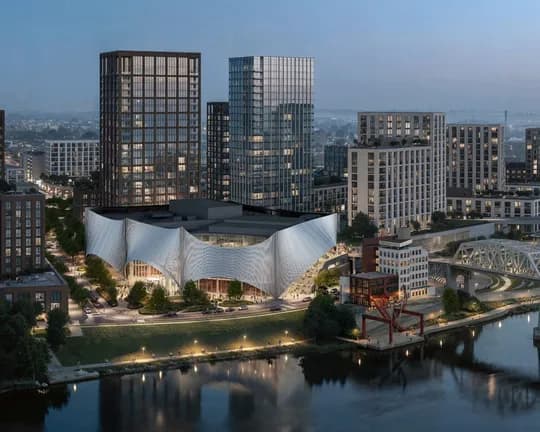 City skyline at dusk featuring glass skyscrapers, a sculptural curved white pavilion by the river, and a bridge.