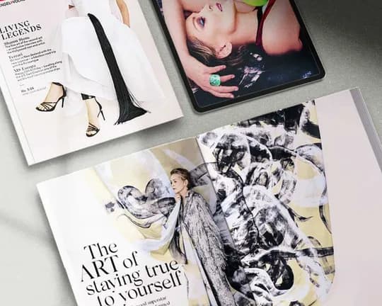 A flat lay photograph of fashion magazines and a tablet on a gray surface, featuring a model, the headline “LIVING LEGENDS,” and abstract art.