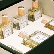 Une série de flacons de parfum en verre, dotés de bouchons nervurés dorés, exposés dans une vitrine ; sur les étiquettes, on peut lire « Master Cedar », « Grey Myrrh » et « After Hours ».