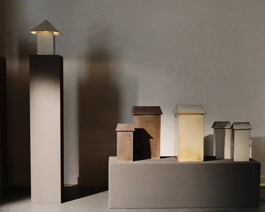 Miniature cityscape: tall dark towers left, small boxy houses with peaked roofs on pedestals, lit from left.
