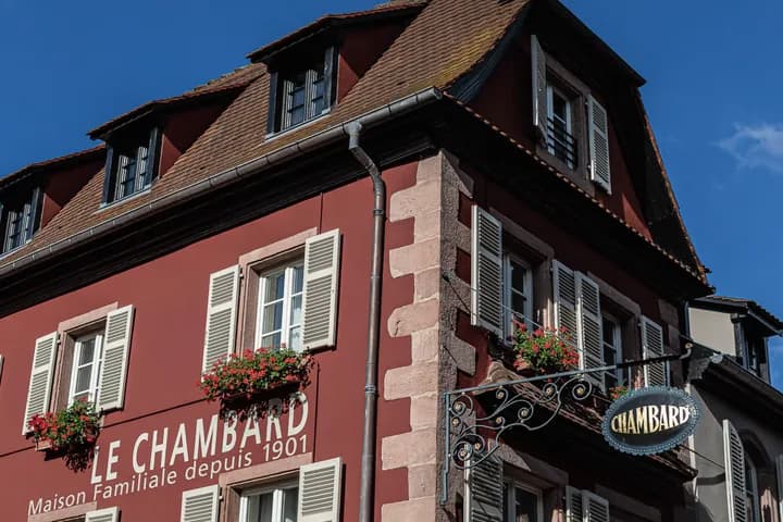 Red European building with white shutters, window flower boxes, and decorative signs, under a clear blue sky.