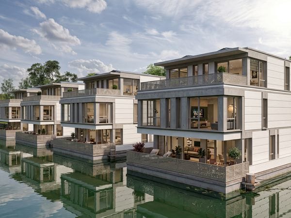Eine Reihe moderner, dreistöckiger Waterfront-Villen mit markanten Glasfassaden und Balkonen, die sich in einem ruhigen, grünen Gewässer unter einem bewölkten Himmel spiegeln.