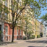 Street view of colorful European-style buildings with trees lining the sidewalk on a sunny day.