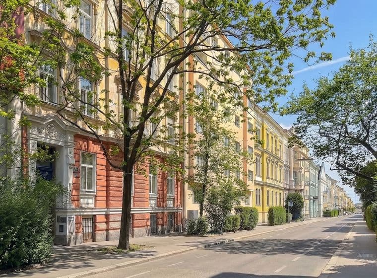 Street view of colorful European-style buildings with trees lining the sidewalk on a sunny day.