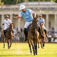 An Italian polo player on a brown horse swings a mallet during a match, with teammates and a cheering crowd in the background.