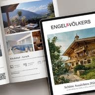 A magazine and a tablet displaying luxury chalet images, alongside a cappuccino with latte art and a stylus on a light gray surface.