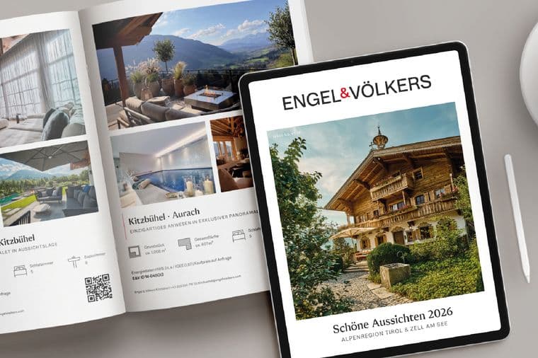 A magazine and a tablet displaying luxury chalet images, alongside a cappuccino with latte art and a stylus on a light gray surface.