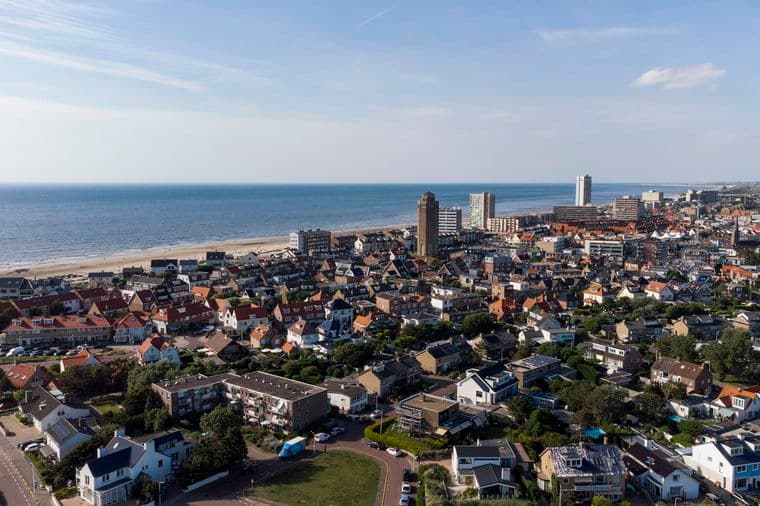 Aerial view of a coastal town with red-roofed houses, a sandy beach, and the blue North Sea under a clear sky.