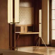 Warm wood-paneled room with a padded quilted wall panel, two tall vertical light fixtures, a wooden desk, and a window showing brick exterior.
