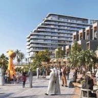 Outdoor plaza by a modern seaside building with people strolling and socializing, featuring palm trees and a giant yellow giraffe sculpture.