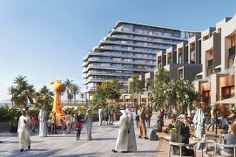 Outdoor plaza by a modern seaside building with people strolling and socializing, featuring palm trees and a giant yellow giraffe sculpture.